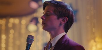 Movie still from “Stargirl” (2020), directed by Julia Hart – A man in a suit holding a microphone in front of his face; Close Up shot, Over the shoulder angle