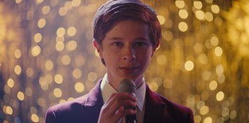 Movie still from “Stargirl” (2020), directed by Julia Hart – A young man holding a microphone in front of a blurry background; Close Up shot, Over the shoulder angle