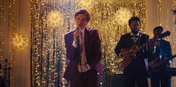 Movie still from “Stargirl” (2020), directed by Julia Hart – A man in a purple suit is singing into a microphone; Medium shot, Over the shoulder angle