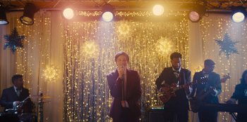 Movie still from “Stargirl” (2020), directed by Julia Hart – A man and a woman singing into microphones in front of lights; Wide shot, Low angle