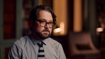 Movie still from “Stephen Curry: Underrated” (2023), directed by Peter Nicks – A man with a beard wearing glasses and a shirt and tie; Close Up shot, High angle