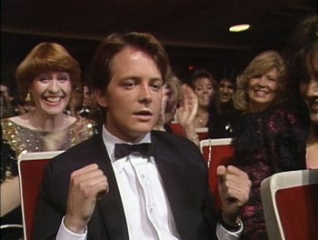 Movie still from “Still: A Michael J. Fox Movie” (2023), directed by Davis Guggenheim – A man wearing a tuxedo and bow tie in front of a group of women; Medium shot, Low angle