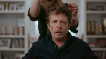 Movie still from “Still: A Michael J. Fox Movie” (2023), directed by Davis Guggenheim – A man getting his hair done by a woman; Close Up shot, Over the shoulder angle