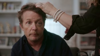 Movie still from “Still: A Michael J. Fox Movie” (2023), directed by Davis Guggenheim – A woman putting a bracelet on a man's head; Close Up shot, Over the shoulder angle