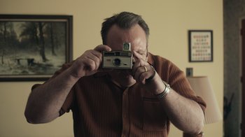 Movie still from “Still: A Michael J. Fox Movie” (2023), directed by Davis Guggenheim – A man taking a picture of himself in the mirror; Close Up shot, Low angle