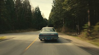 Movie still from “Still: A Michael J. Fox Movie” (2023), directed by Davis Guggenheim – A car driving down a road near some trees; Wide shot, High angle