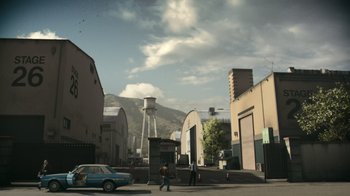 Movie still from “Still: A Michael J. Fox Movie” (2023), directed by Davis Guggenheim – People walking down a street near a building and a water tower; Extreme Wide shot, High angle