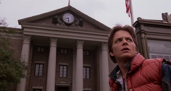 Movie still from “Still: A Michael J. Fox Movie” (2023), directed by Davis Guggenheim – A man standing in front of a building with an american flag; Medium shot, Low angle