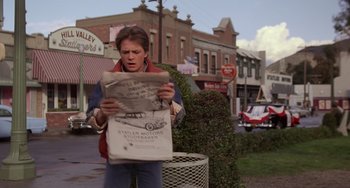 Movie still from “Still: A Michael J. Fox Movie” (2023), directed by Davis Guggenheim – A man standing on the side of the street holding a newspaper; Medium shot, Over the shoulder angle