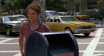 Movie still from “Still: A Michael J. Fox Movie” (2023), directed by Davis Guggenheim – A man standing next to a mailbox on the side of the street; Medium shot, Over the shoulder angle