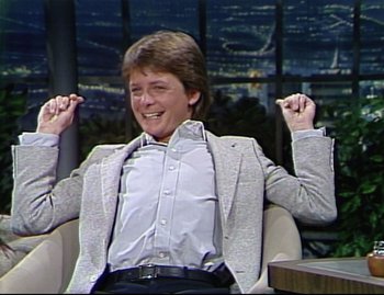 Movie still from “Still: A Michael J. Fox Movie” (2023), directed by Davis Guggenheim – A young man sitting in a chair with his arms raised; Medium shot, High angle