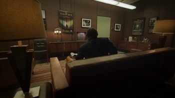 Movie still from “Still: A Michael J. Fox Movie” (2023), directed by Davis Guggenheim – A man sitting on a couch reading a book in front of a television; Wide shot, High angle