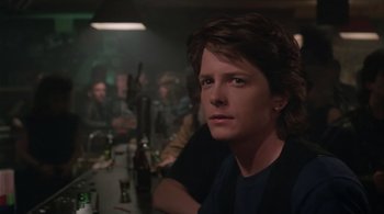 Movie still from “Still: A Michael J. Fox Movie” (2023), directed by Davis Guggenheim – A man sitting in front of a group of people at a bar; Close Up shot, Over the shoulder angle
