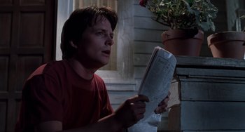 Movie still from “Still: A Michael J. Fox Movie” (2023), directed by Davis Guggenheim – A man sitting on the ground reading a newspaper; Close Up shot, Low angle