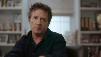 Movie still from “Still: A Michael J. Fox Movie” (2023), directed by Davis Guggenheim – A person sitting in a chair; Close Up shot, Over the shoulder angle