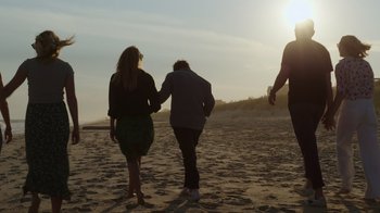 Movie still from “Still: A Michael J. Fox Movie” (2023), directed by Davis Guggenheim – Two people holding hands while walking on the beach; Wide shot, Low angle