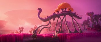 Movie still from “Strange World” (2022), directed by Don Hall – An animated scene of a giant creature with a person standing next to it in a field; Extreme Wide shot, Over the shoulder angle