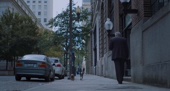 Movie still from “Strays” (2023), directed by Josh Greenbaum – A man walking a dog down a street; Wide shot, Low angle