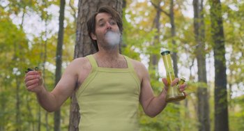 Movie still from “Strays” (2023), directed by Josh Greenbaum – A man in a yellow shirt is smoking a cigarette and holding a bottle; Medium shot, Low angle