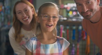 Movie still from “Strays” (2023), directed by Josh Greenbaum – A young girl wearing glasses and smiling for the camera; Close Up shot, Over the shoulder angle