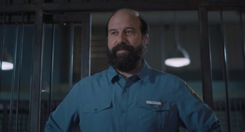 Movie still from “Strays” (2023), directed by Josh Greenbaum – A man with a goatee and beard wearing a blue shirt; Medium shot, Over the shoulder angle