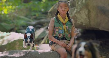 Movie still from “Strays” (2023), directed by Josh Greenbaum – A young girl sitting on a rock next to a black and white dog; Medium shot, Low angle