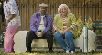 Movie still from “Strays” (2023), directed by Josh Greenbaum – A man and a woman sitting next to each other on top of a bench; Medium shot, High angle