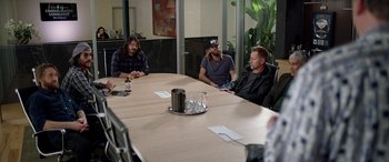 Movie still from “Studio 666” (2022), directed by BJ McDonnell – A group of people sitting around a table; Wide shot, High angle