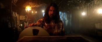 Movie still from “Studio 666” (2022), directed by BJ McDonnell – A man with long black hair and a plaid shirt; Medium shot, Low angle