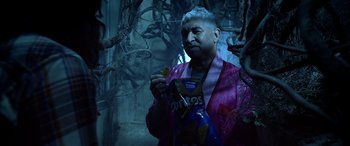 Movie still from “Studio 666” (2022), directed by BJ McDonnell – A man in a pink robe holding a bag of potato chips; Medium shot, High angle