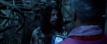 Movie still from “Studio 666” (2022), directed by BJ McDonnell – A man with long black hair is talking to someone; Medium shot, Over the shoulder angle