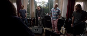 Movie still from “Studio 666” (2022), directed by BJ McDonnell – A group of people standing around a room; Wide shot, Over the shoulder angle