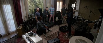 Movie still from “Studio 666” (2022), directed by BJ McDonnell – A group of people standing around a living room; Wide shot, High angle