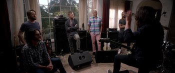 Movie still from “Studio 666” (2022), directed by BJ McDonnell – A group of people standing around a room with guitars; Wide shot, Over the shoulder angle