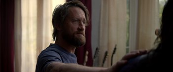 Movie still from “Studio 666” (2022), directed by BJ McDonnell – A man with long hair and a beard is sitting in front of a window; Close Up shot, Over the shoulder angle