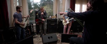 Movie still from “Studio 666” (2022), directed by BJ McDonnell – A group of people that are sitting in a living room; Medium shot, Over the shoulder angle