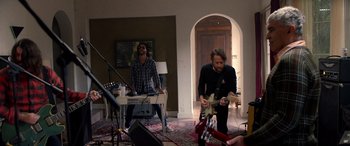 Movie still from “Studio 666” (2022), directed by BJ McDonnell – A group of people playing instruments in a room; Wide shot, Over the shoulder angle