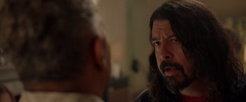 Movie still from “Studio 666” (2022), directed by BJ McDonnell – A man with long hair talking to another man in a room; Close Up shot, Over the shoulder angle