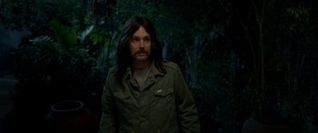 Movie still from “Studio 666” (2022), directed by BJ McDonnell – A man with long black hair standing in the woods; Medium shot, Over the shoulder angle