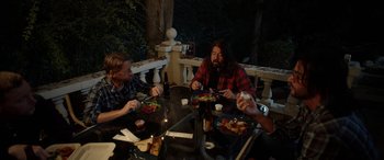 Movie still from “Studio 666” (2022), directed by BJ McDonnell – A group of people sitting at a table eating food; Medium shot, High angle