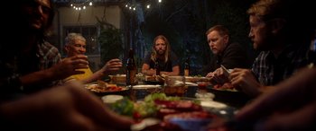 Movie still from “Studio 666” (2022), directed by BJ McDonnell – A group of people sitting at a table with plates of food; Medium shot, Over the shoulder angle