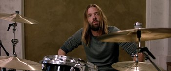 Movie still from “Studio 666” (2022), directed by BJ McDonnell – A man with long hair is playing drums; Close Up shot, High angle