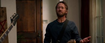 Movie still from “Studio 666” (2022), directed by BJ McDonnell – A man with long hair and a beard is holding a guitar; Medium shot, Over the shoulder angle