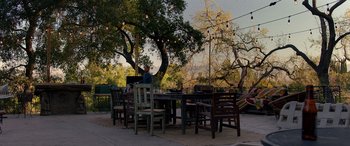 Movie still from “Studio 666” (2022), directed by BJ McDonnell – A man sitting at a table in front of an outdoor dining area; Extreme Wide shot, High angle