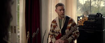 Movie still from “Studio 666” (2022), directed by BJ McDonnell – A man with a beard is holding a guitar; Medium shot, Over the shoulder angle