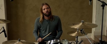 Movie still from “Studio 666” (2022), directed by BJ McDonnell – A man with long hair is playing drums; Close Up shot, High angle