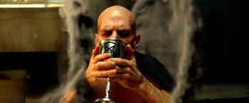 Movie still from “Studio 666” (2022), directed by BJ McDonnell – A bald man drinking from a metal cup; Close Up shot, Low angle