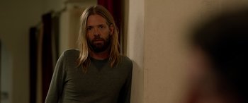 Movie still from “Studio 666” (2022), directed by BJ McDonnell – A man with long blonde hair wearing a gray shirt; Medium shot, Low angle