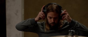Movie still from “Studio 666” (2022), directed by BJ McDonnell – A man with long blond hair wearing headphones; Close Up shot, High angle