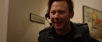 Movie still from “Studio 666” (2022), directed by BJ McDonnell – A man wearing a headset in front of a sign; Close Up shot, Over the shoulder angle